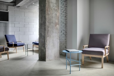Work zone in the office in a loft style with a concrete column and light walls. Near the column there are multi-colored armchairs with wooden legs and small round metal tables with a laptop.
